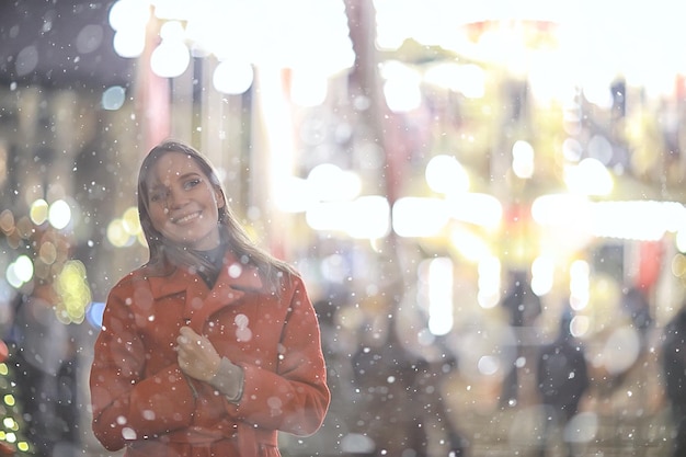 Promenade de Noël dans la ville / une fille adulte se promène dans la ville nocturne par une nuit de fête, les lumières de la ville sont le nouvel an