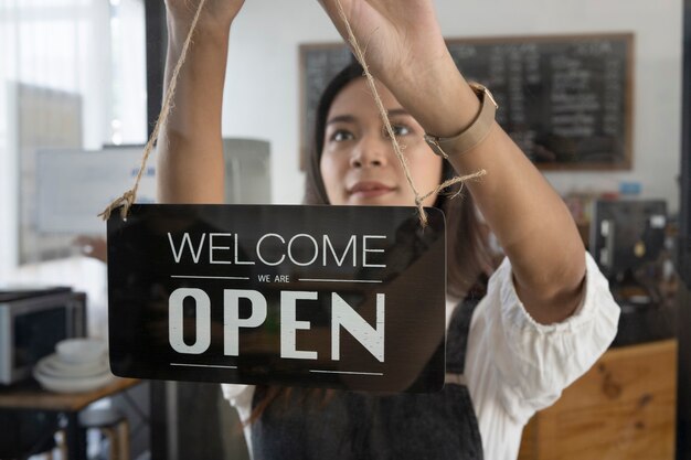 Propriétaire de café femme accrochant le signe ouvert sur une porte en verre.