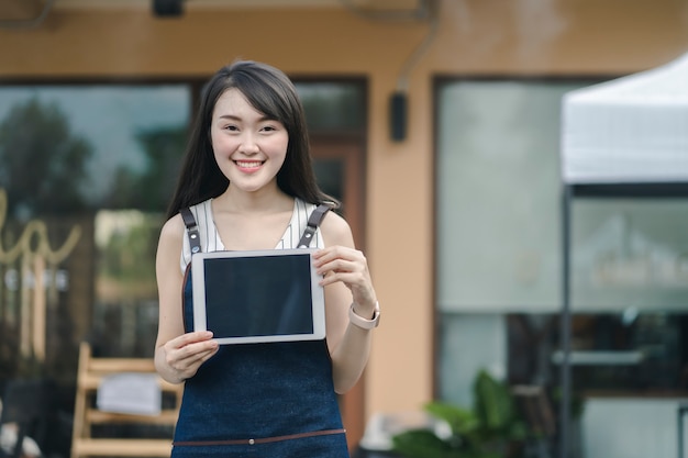 Propriétaire d'entreprise debout à l'entrée tenant la tablette écran vide