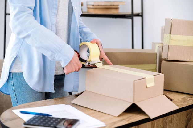 Propriétaire d'entreprise utilisant du scotch et des ciseaux pour emballer la boîte