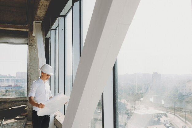 Propriétaire masculin regardant le plan près d'une grande fenêtre de son immeuble en construction.