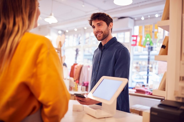 Propriétaire de petite entreprise féminine acceptant le paiement sans contact dans la boutique du client à l'aide d'un téléphone mobile