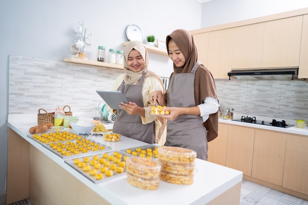 Propriétaire d'une petite entreprise musulmane fabriquant une collation nastar maison à vendre. belle femme asiatique avec partenaire cuisine et tenant tablet pc