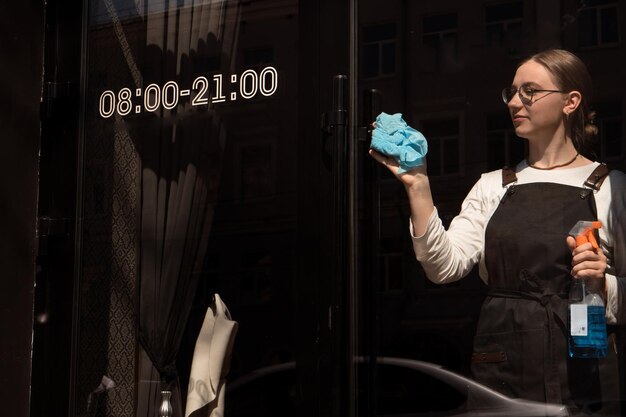 Propriétaire de petite entreprise en tablier nettoyant le verre de la porte du café