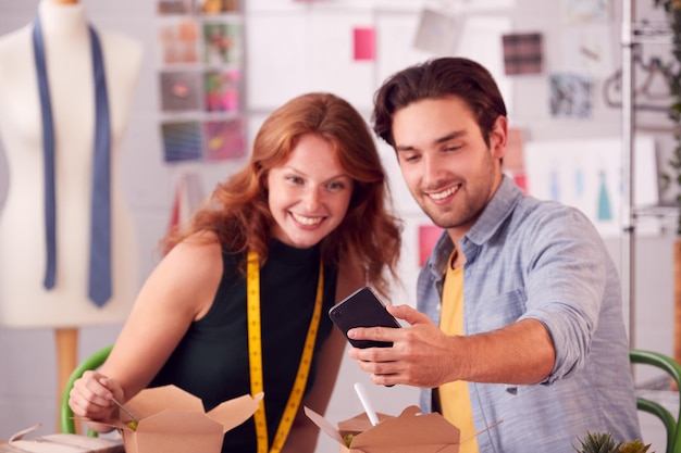 Propriétaires d'entreprises de mode masculins et féminins ayant un déjeuner de travail regardant un téléphone portable en studio