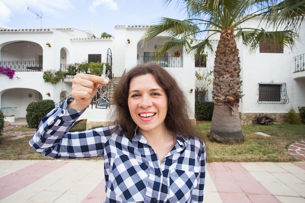 Propriété, immobilier, achat et location concept - Femme avec clés debout à l'extérieur de la nouvelle maison