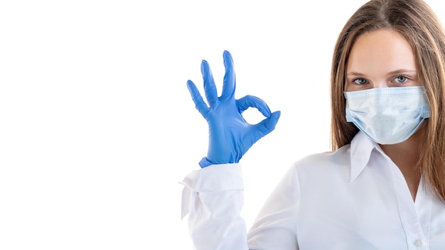 Protection contre la pandémie Geste Ok Beau travail Femme en gants de masque de médecine montrant le signe d'approbation en regardant la caméra isolé espace de copie blanche Fond de publicité