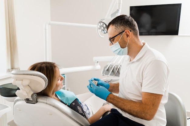 Prothèses et implants dentaires Un médecin dentiste montre une mâchoire artificielle en plastique avec des implants dentaires Consultation de prothèses dentaires avec un dentiste pour une patiente en dentisterie