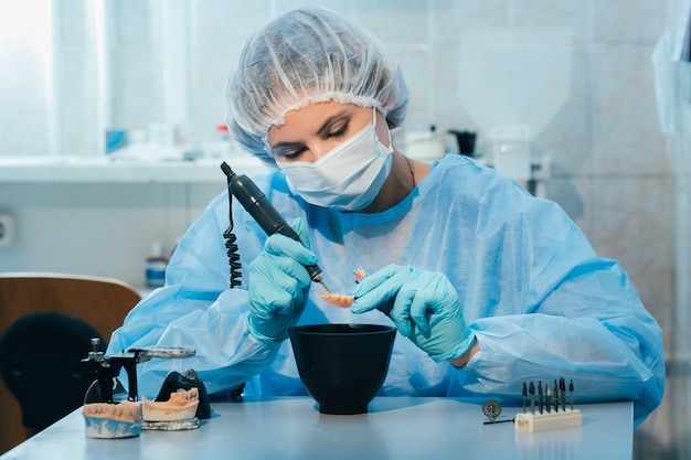 Un prothésiste dentaire masqué et ganté travaille sur une dent prothétique dans son laboratoire.