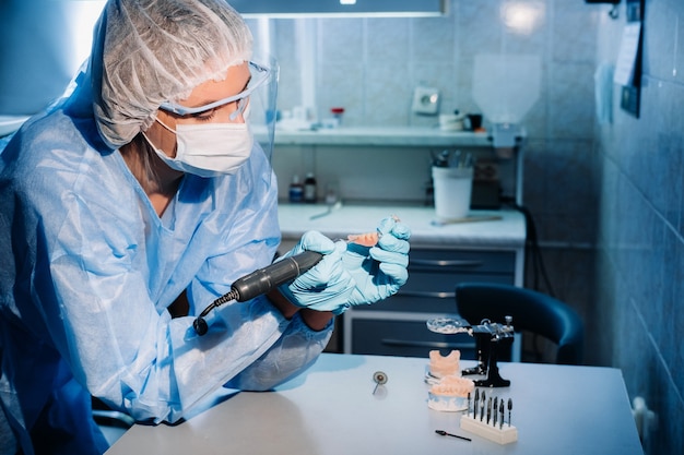 Un prothésiste dentaire masqué et ganté travaille sur une dent prothétique dans son laboratoire.