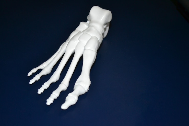 Photo prototype blanc du squelette du pied humain imprimé sur une imprimante 3d sur une surface sombre. modélisation des dépôts fondus, fdm. technologie additive moderne et progressive. concept de la révolution industrielle 4.0