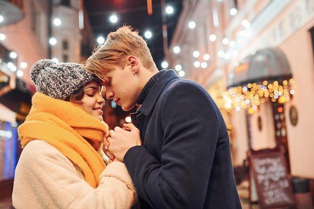 Proximité des gens. Heureux jeune couple dans des vêtements chauds est ensemble dans la rue décorée de Noël.