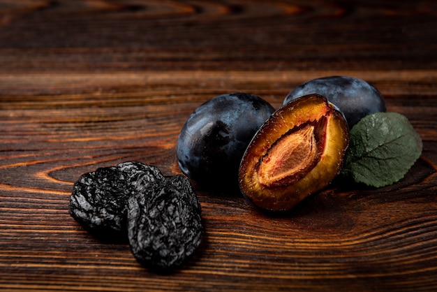 Prune fraîche et pruneau sur fond de bois foncé.