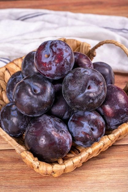 Photo prune noire sur fond de bois une pile de prunes noires dans un panier de près