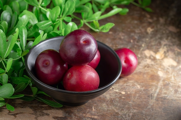 Prune rouge cerise avec des feuilles vertes sur fond en bois