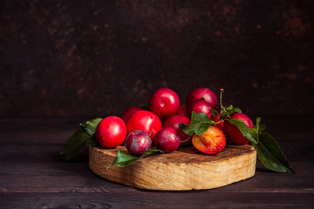 Prune rouge fraîche avec des feuilles sur un fond sombre en bois