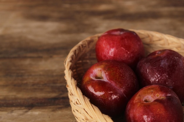 Prune rouge mise dans un panier en bambou noir sur un plancher en bois