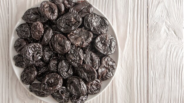 Les pruneaux frais, un ingrédient pour une alimentation saine. Prunes séchées dans une assiette en céramique blanche sur une table rustique en bois.