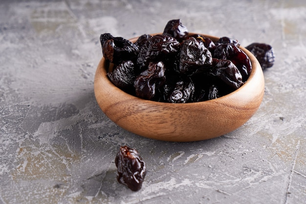 Pruneaux, prunes séchées dans un bol en bois sur une table grise Style rustique