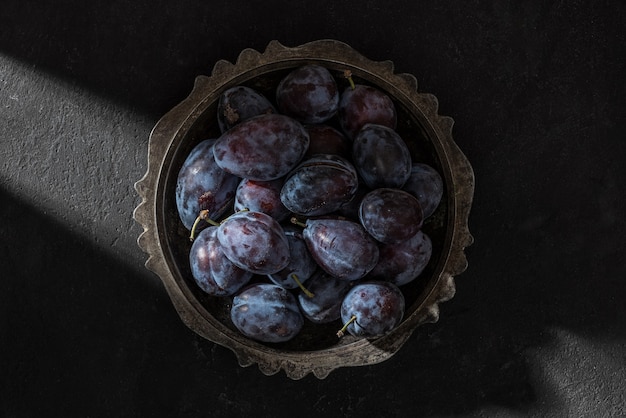 Prunes bleues mûres fraîches dans un bol dans le rayon de lumière sur fond noir. Tir créatif. vue de dessus