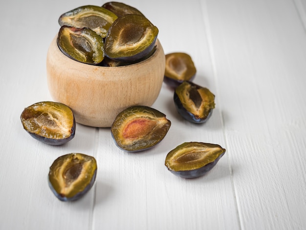 Prunes coupées en deux dans un bol sur un bureau vintage blanc.