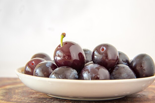 Prunes fraîches dans une assiette avec des gouttes d'eau sur fond blanc