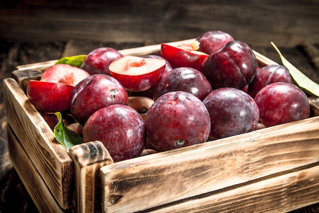 Prunes fraîches dans une boîte en bois. Sur une table en bois.