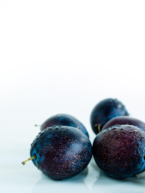 Prunes fraîches avec une prune coupée sur fond blanc.