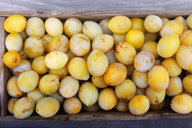 Prunes jaunes fraîches. Fruits mûrs dans une boîte en bois sur fond de planches.