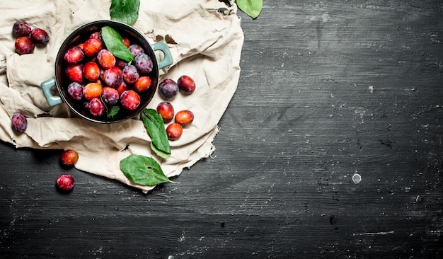 Prunes mûres dans un bol avec des feuilles sur un tableau noir.