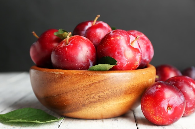 Des prunes mûres dans un bol sur une table en bois sur un fond sombre
