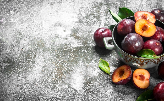 Prunes mûres dans un bol. Sur une table rustique.