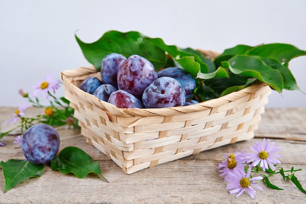 Prunes mûres dans un panier de paille sur une table en bois rustique