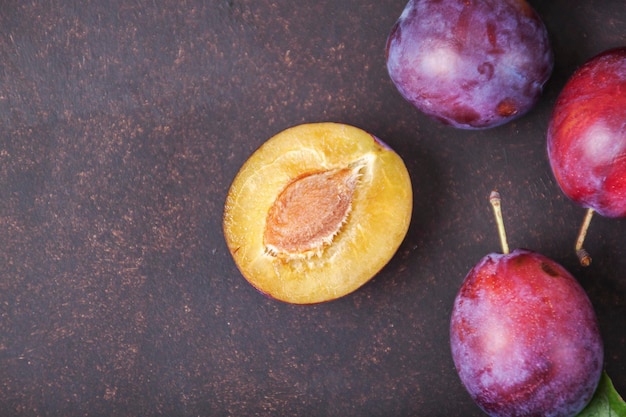 Prunes mûres avec des feuilles sur la table. Fond de fruits d'été. Dessus vue prune, pose à plat