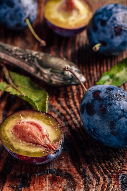 Prunes mûres sur table en bois avec feuilles, gouttes d'eau et couteau vintage