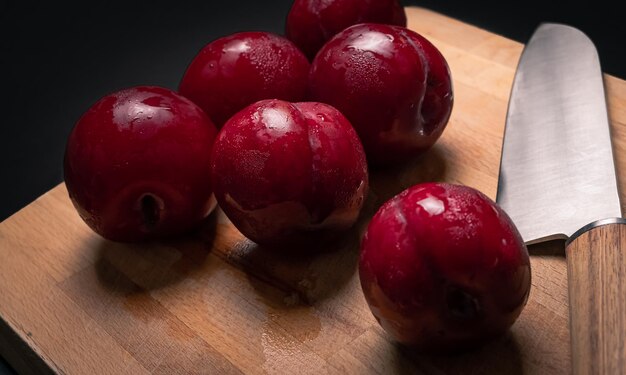 Prunes rouges sur planche à pain avec couteau et fond noir