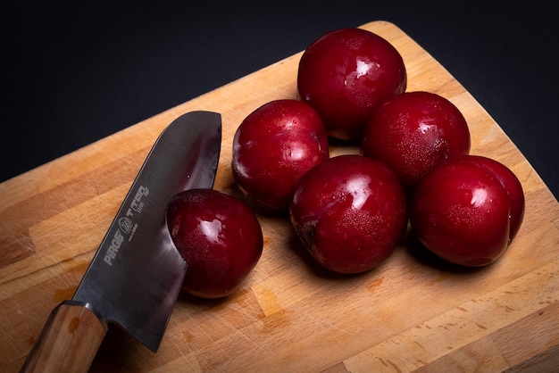 Prunes rouges sur planche à pain avec couteau et fond noir