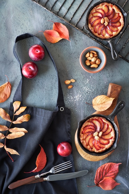 Prunes rouges et tartes aux prunes en fonte sur un tablier de cuisine noir jeté sur gris