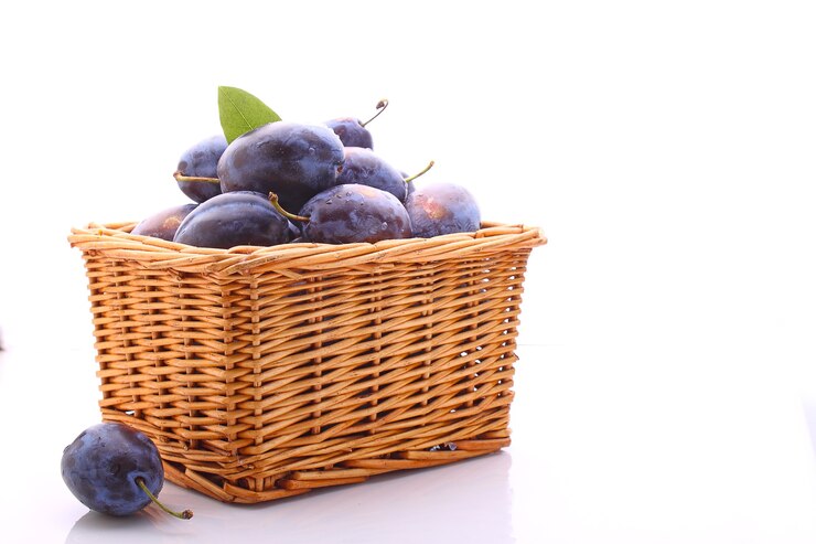 Prunes violettes dans un panier en osier sur fond blanc