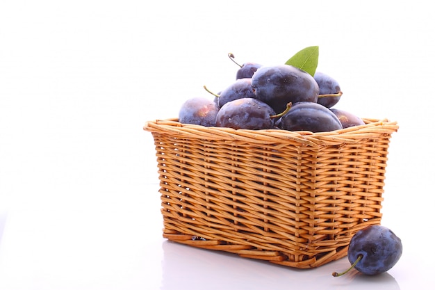 Prunes violettes dans un panier en osier sur fond blanc