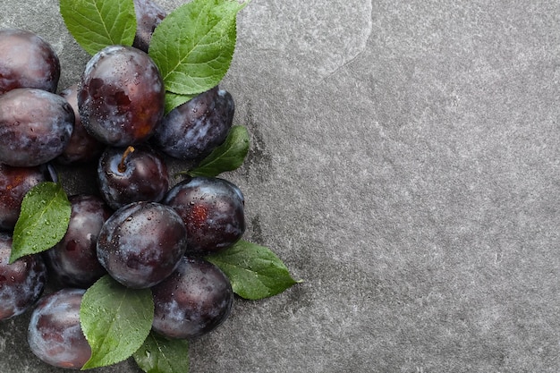 Prunes violettes mûres avec des feuilles sur une table en pierre