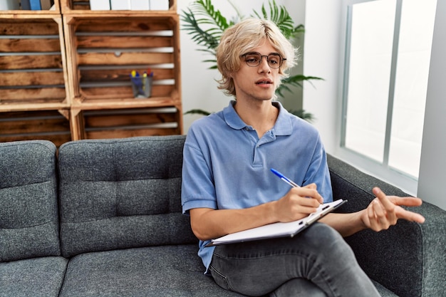 Psychologue de jeune homme blond écrivant sur un document parlant à la clinique de psychologie