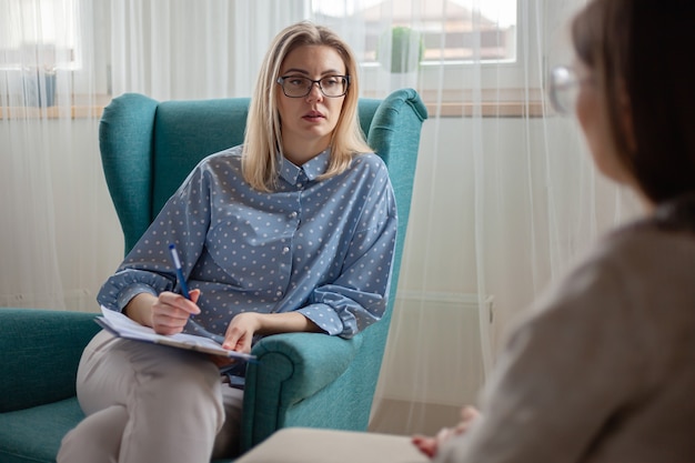 La psychothérapeute de femme consulte le patient s'asseyant dans le fauteuil