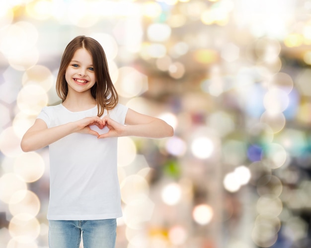 publicité, enfance, charité, vacances et personnes - fille souriante en t-shirt blanc faisant un geste en forme de coeur sur fond étincelant