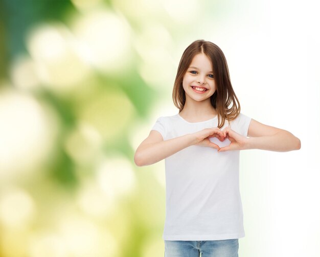 publicité, enfance, écologie, charité et personnes - petite fille souriante en t-shirt blanc faisant un geste en forme de coeur sur fond vert