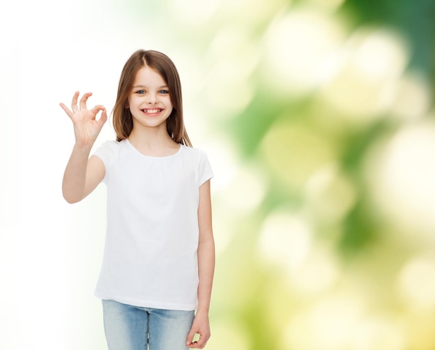 publicité, enfance, geste, écologie et personnes - petite fille souriante en t-shirt blanc vierge montrant le signe ok sur fond vert