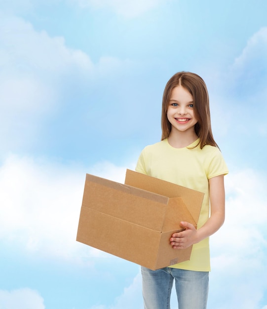 publicité, enfance, livraison, courrier et personnes - petite fille souriante tenant une boîte en carton ouverte sur fond nuageux