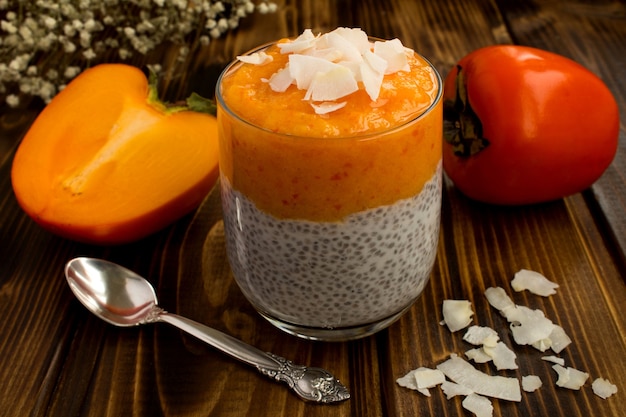 Pudding au chia, kaki et copeaux de noix de coco sur le fond en bois brun