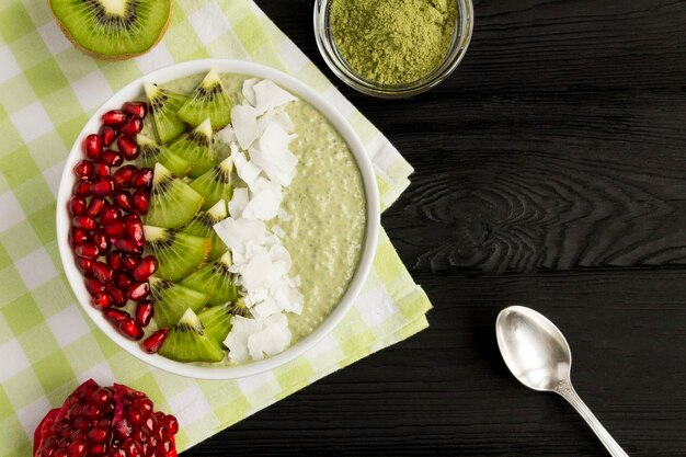 Pudding au chia, thé matcha, kiwi, graines de grenade et flocons de noix de coco dans le bol blanc sur la table en bois noire. Vue de dessus. Copiez l'espace.