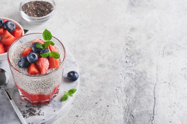 Pudding aux fraises chia Petit-déjeuner végétalien sain pouding aux graines de chia avec baies fraîches et menthe en verre sur fond de béton gris